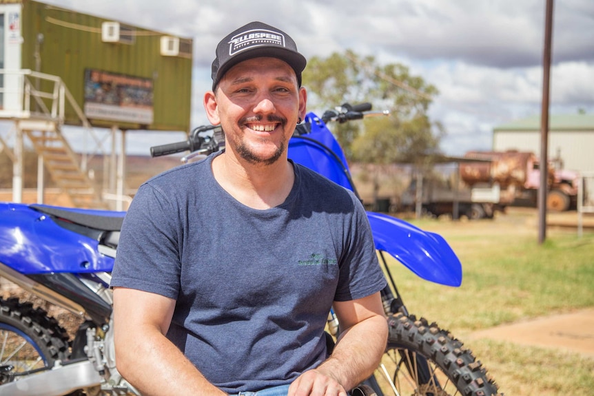 A man sits in front of a dirt bike.