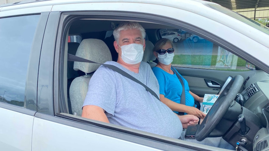 A man and a woman sit in a car wearing face masks.