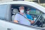 A man and a woman sit in a car wearing face masks.