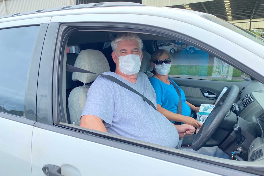 A middle-aged man and woman wearing face masks sit in a car