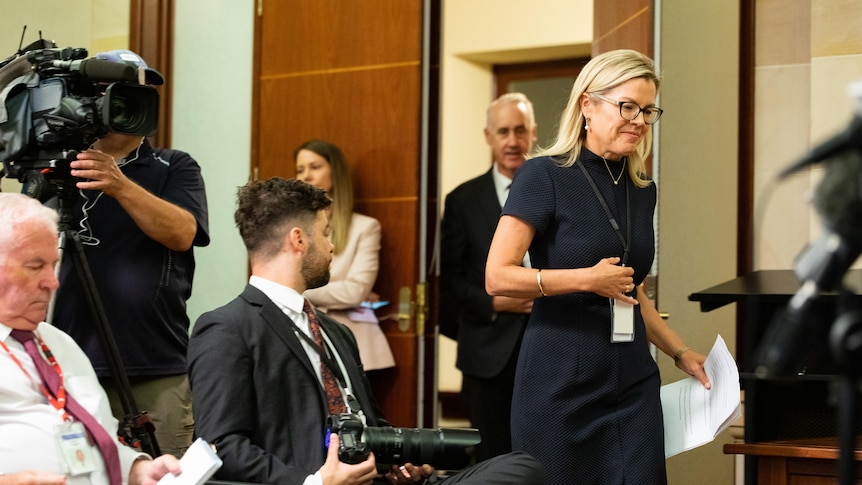 People walk through a door past seated journalists