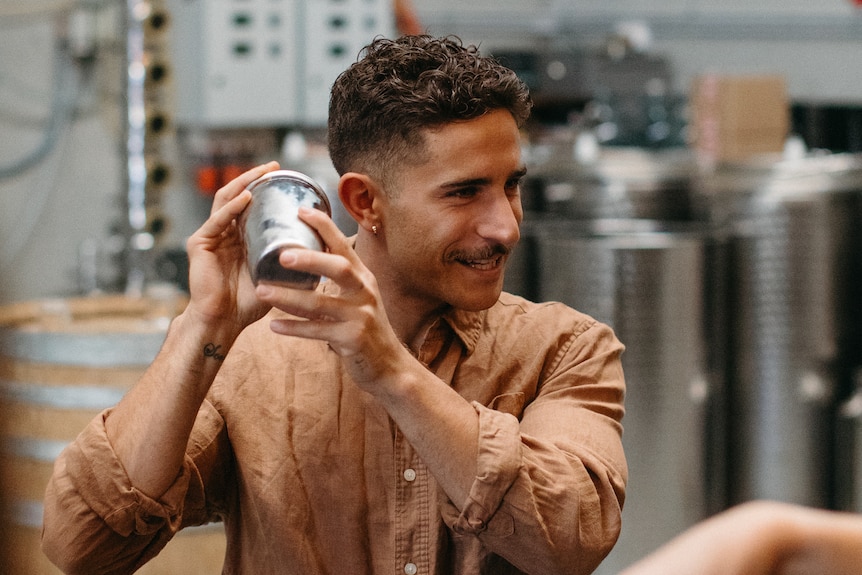 A man in a light brown shirt shakes a cocktail shaker.