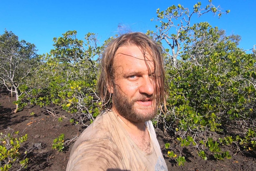 A muddied man stands in the mangroves.