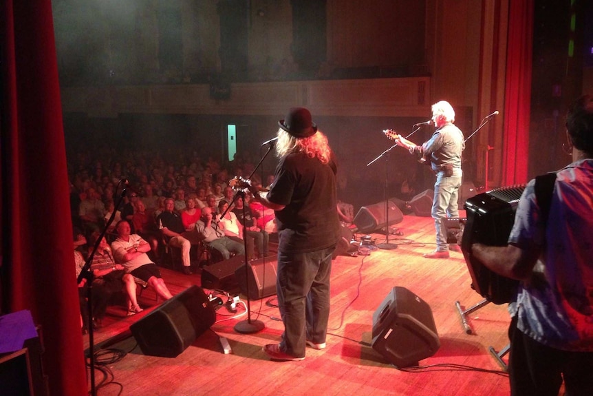 Two musicians, seen from behind, play a live gig on a stage.