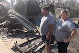 Angelo and Chantal standing from of twisted metal looking at the wreckage of their burnt out house.