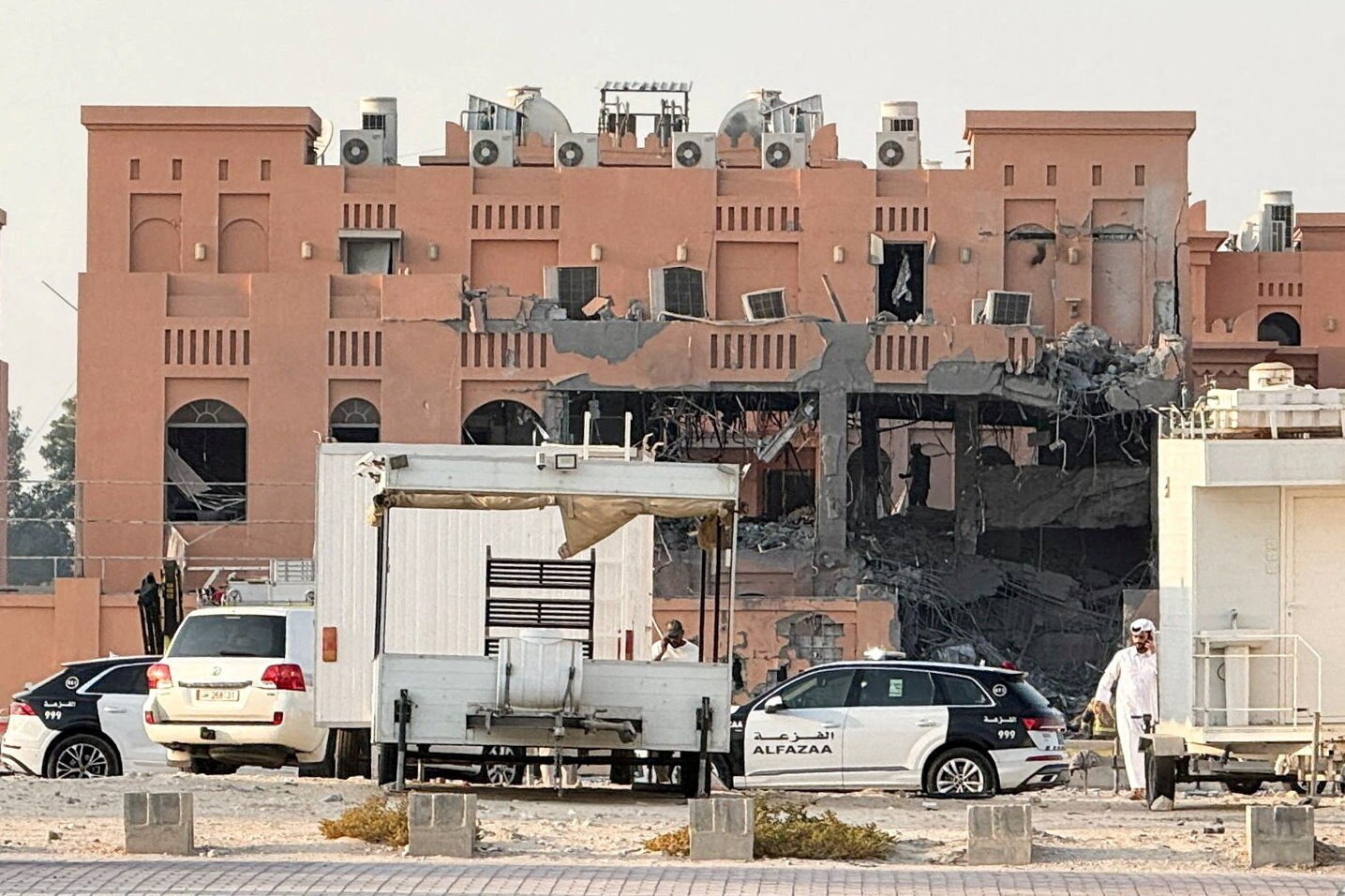 A damaged building with trucks and cars parked in front of it 