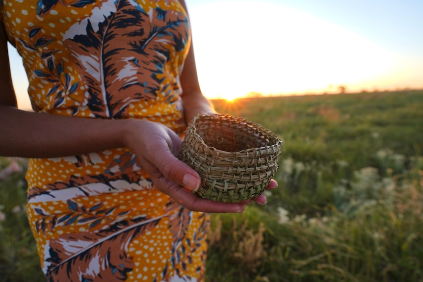 Woman holding basket in field at sunset