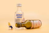 A photo miniature people sitting on alcohol bottles.
