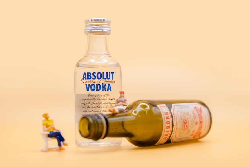 A photo miniature people sitting on alcohol bottles.