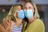 A mother and daughter stand hugging wearing face masks and posing for a photo inside Perth Airport.