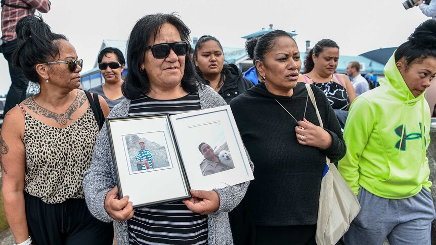 A woman holds up photos of two victims of the White Island volcano explosion