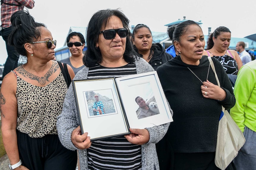 A woman holds up photos of two victims of the White Island volcano explosion