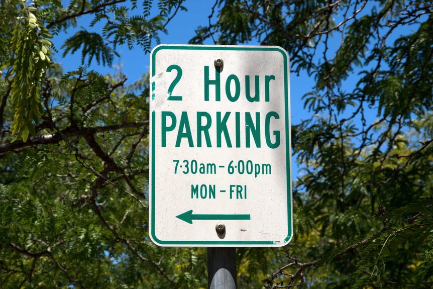 Sign saying '2 hour parking' against a blurred backdrop of trees.