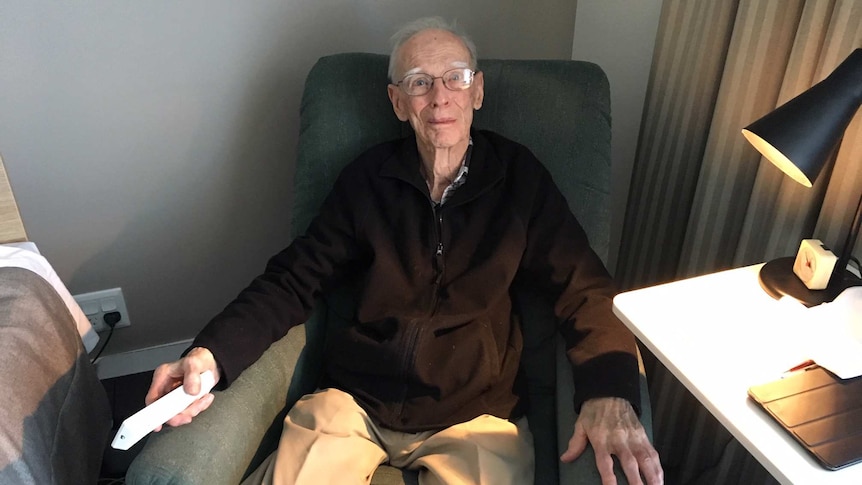 An elderly man sitting in a chair holding a remote control