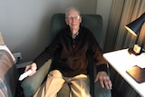 An elderly man sitting in a chair holding a remote control