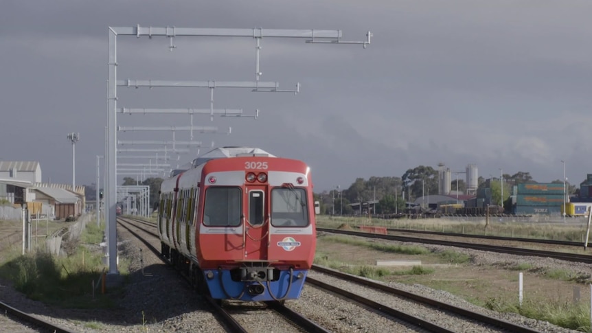 A small red train passes under steel structures