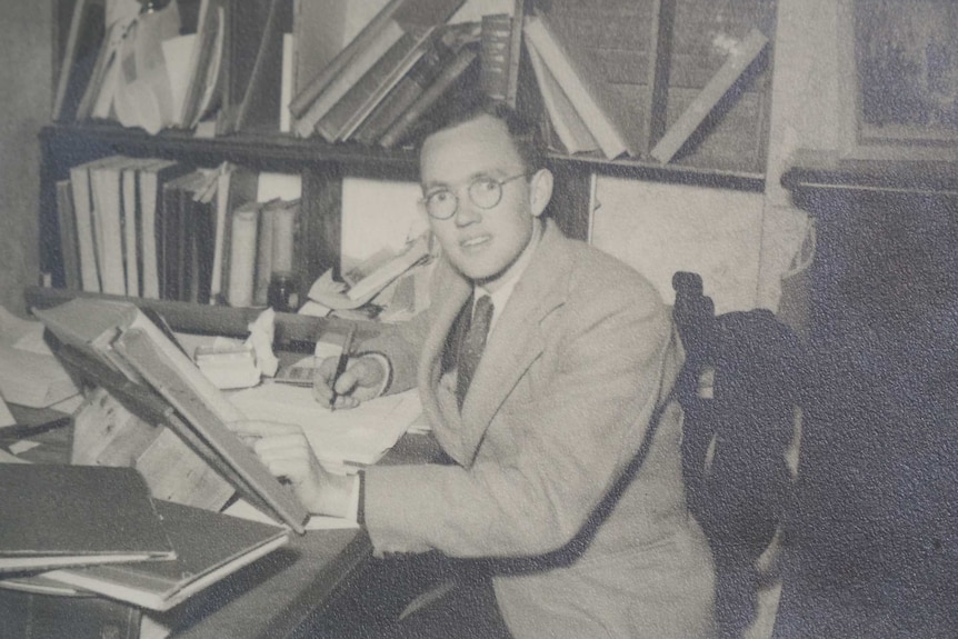 A black and white image of Stan McKay in his 20s, studying while surrounded by books