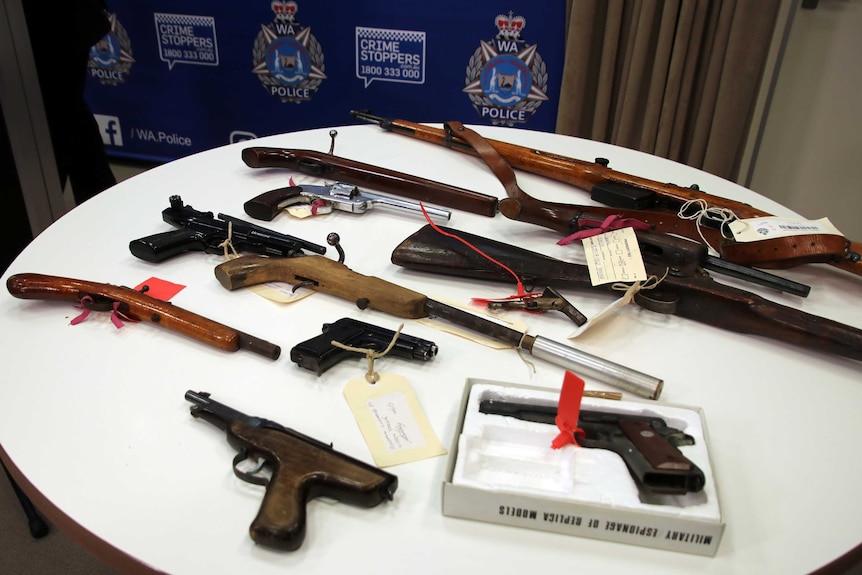 A range of different types of firearms spread out on a table.