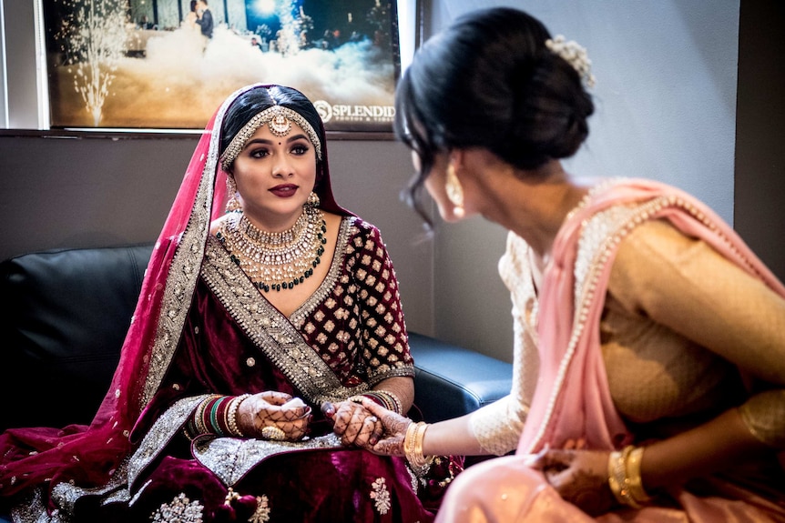 A woman in a dark maroon sari sits underneath a poster showing a Christian wedding.