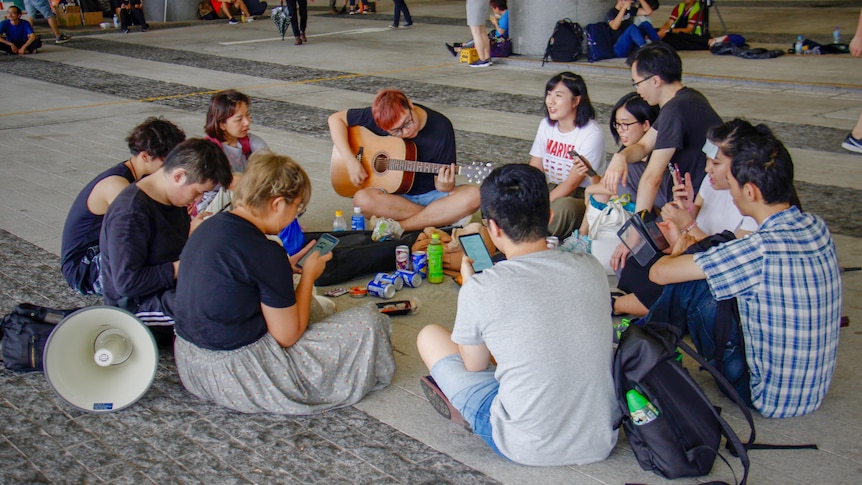A group of young people sitting in a circle with a guitar and a loud speaker near them