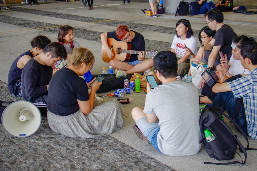 A group of young people sitting in a circle with a guitar and a loud speaker near them