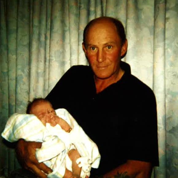 An old photo of a man in a black shirt holding a baby. 