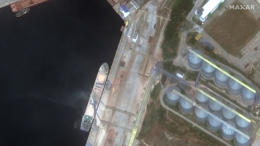 A satellite image of a ship docked next to a shoreline at night with two buildings nearby