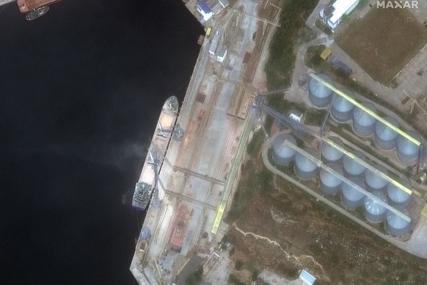 A satellite image of a ship docked next to a shoreline at night with two buildings nearby