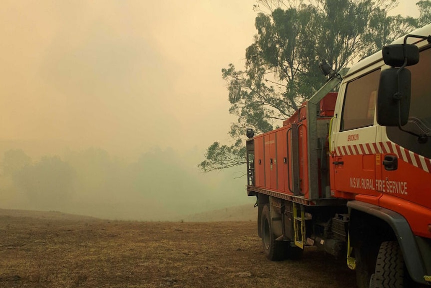 A fire truck in bushland in front of a smoky backdrop.