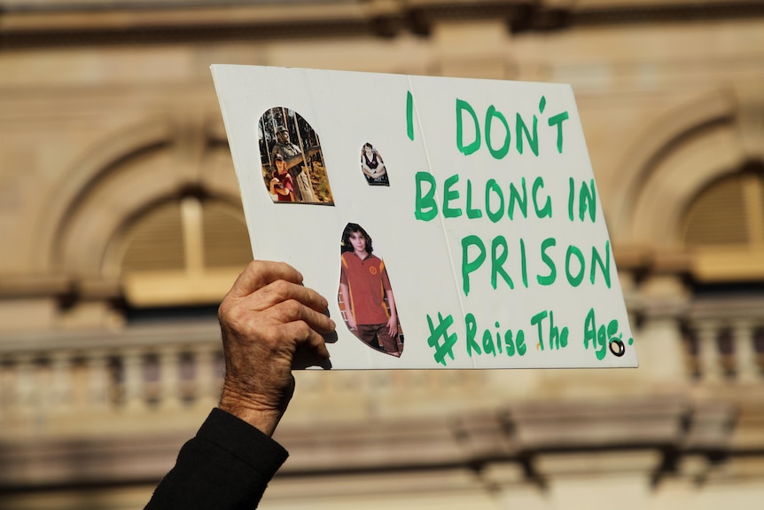 A hand holds a sign saying 'I don't belong in prison'