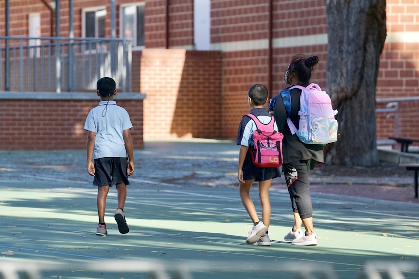 Three primary school students walk across a courtyard.
