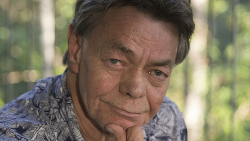 A man rests his chin on his hand looking at the camera.