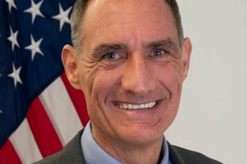 A portrait photo of Michael Goldman with a US flag in the background.