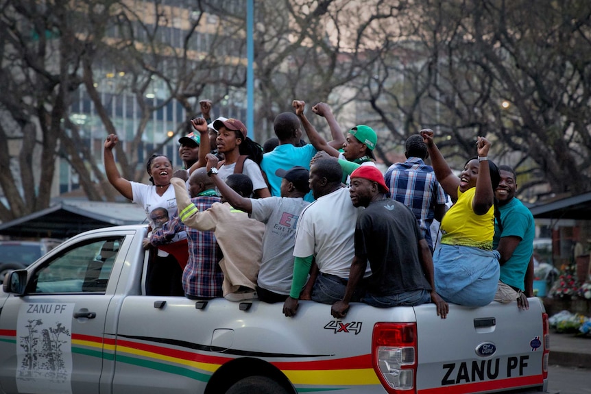 A ute filled with people celebrating, with arms raised, cheering. The ute has the words Zanu PF written on it.
