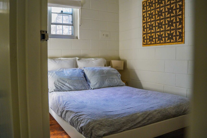 A double bed in a small stone-walled room with a tiny window and a painting on the wall