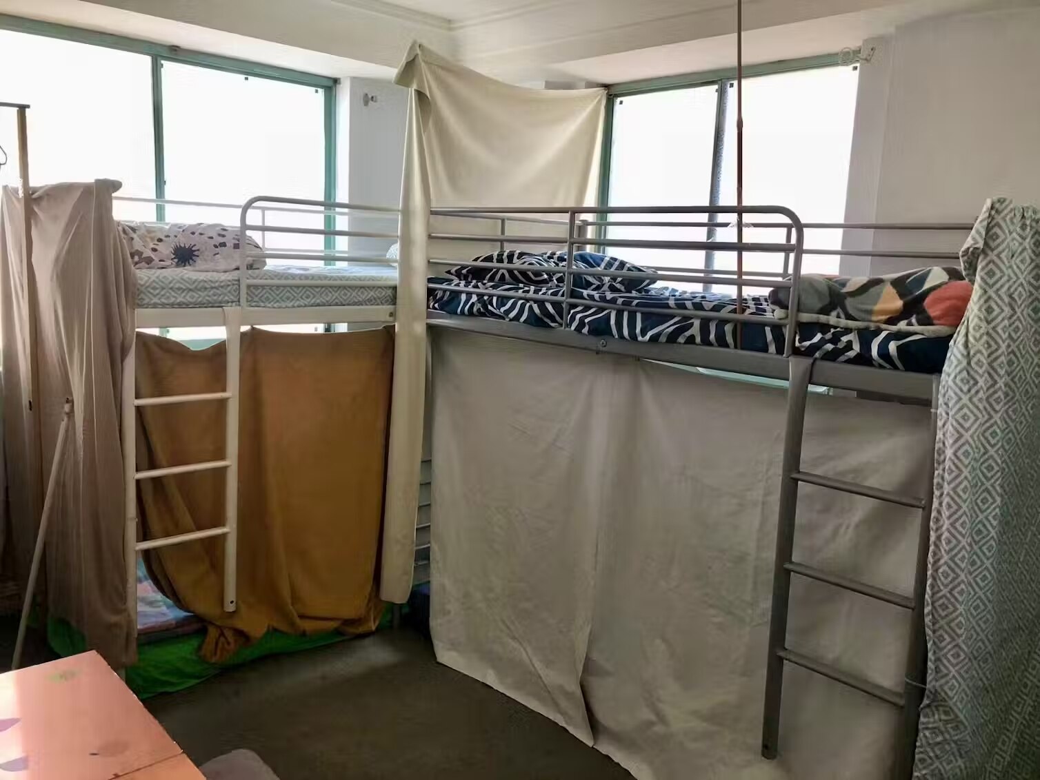 A photo of a small, windowed bedroom with two bunk beds which have sheets and curtains strung up between them