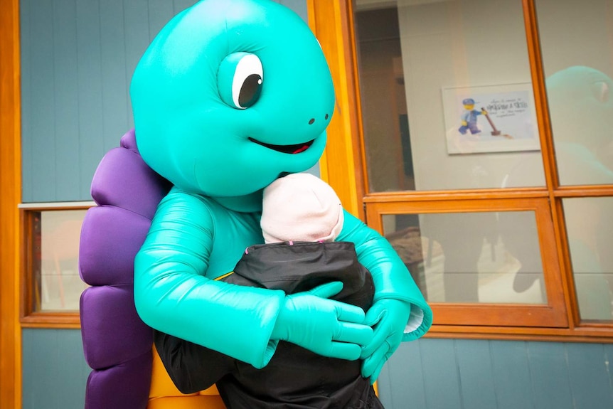 A blue turtle mascot hugs a young woman with Down's syndrome.