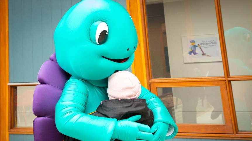 A blue turtle mascot hugs a young woman with Down's syndrome.