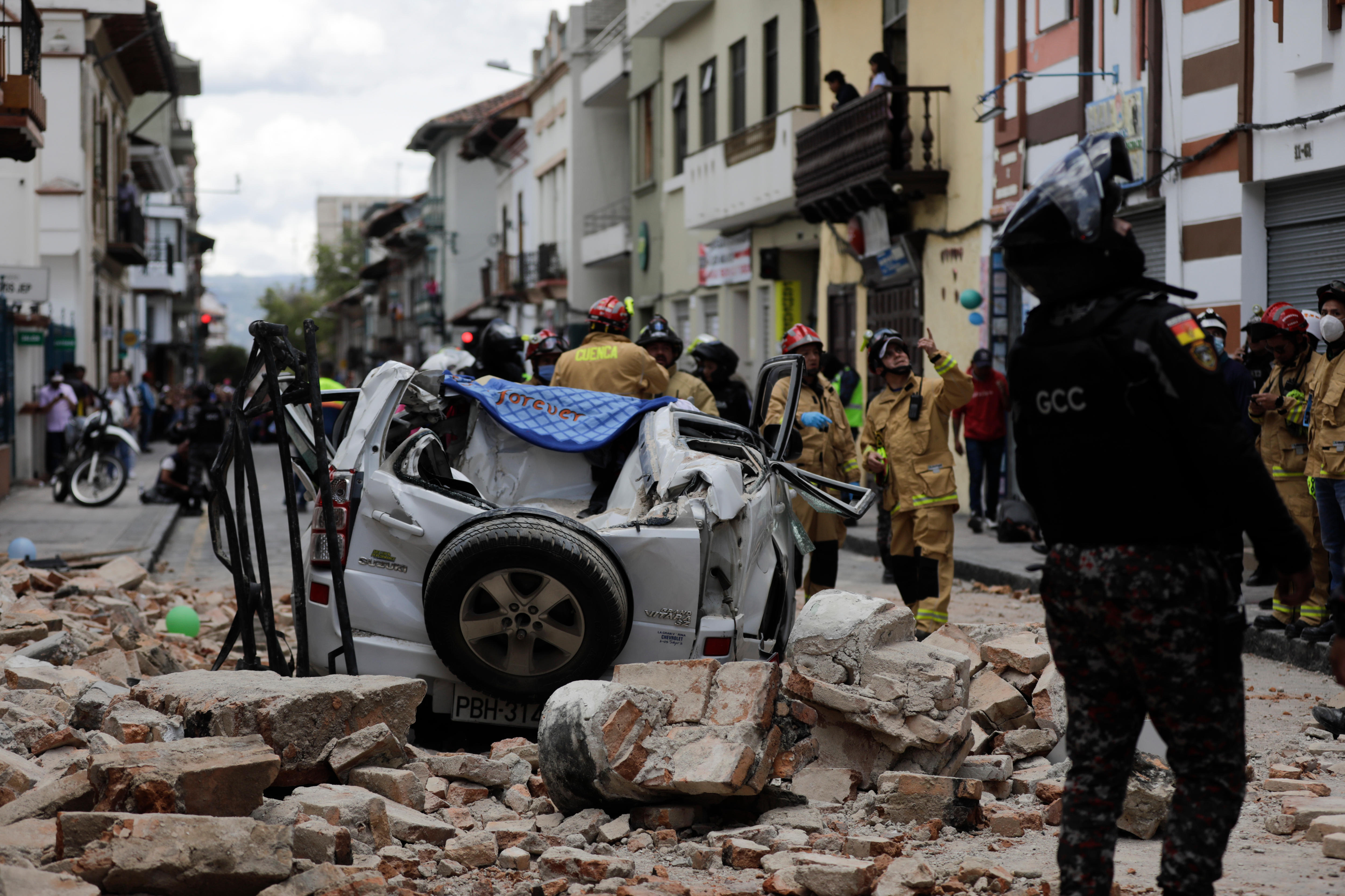 A police officer looks up next to a car crushed by debris after an earthquake.