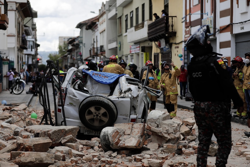 A police officer looks up next to a car crushed by debris after an earthquake.