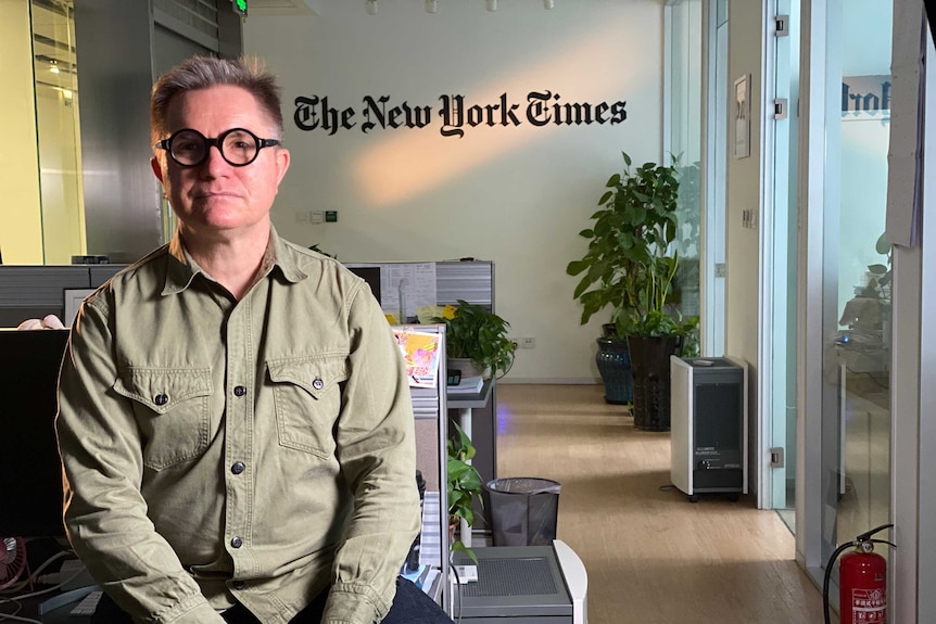 Chris Buckley sitting in his office with the New York Times branding on the wall