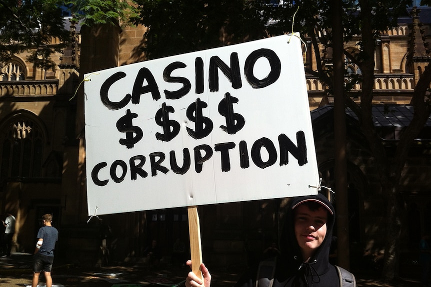 A young man holds up a sign saying "Casino $$$ Corruption'