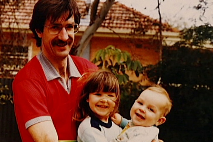 A man in his fifties with two small children outside a house.