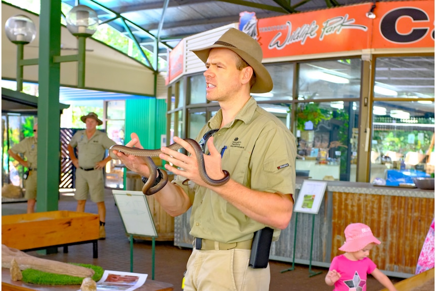 Man in ranger uniform holding a snake under an undercroft.