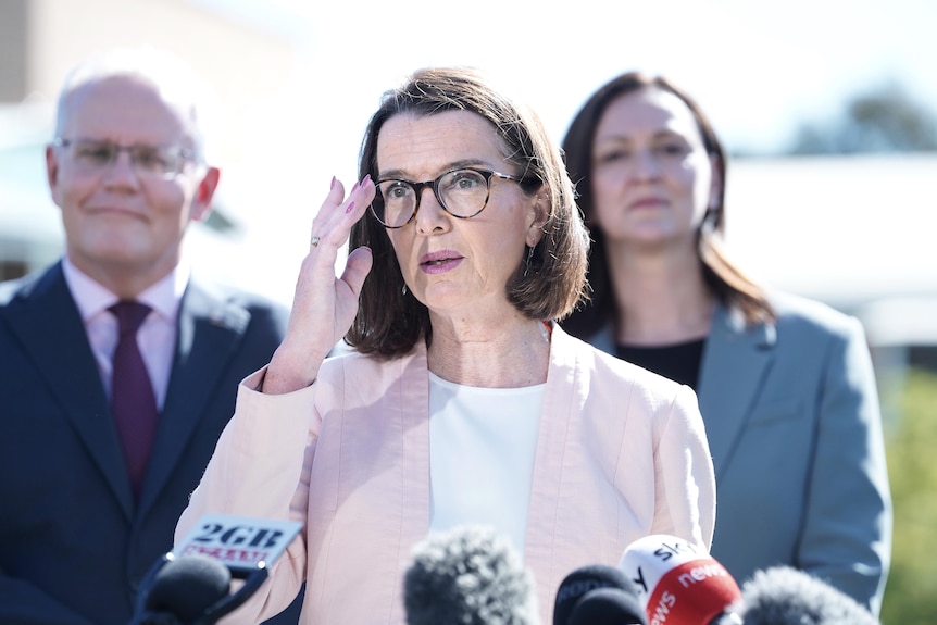 Anne Ruston touches her glasses while standing at a press conference 