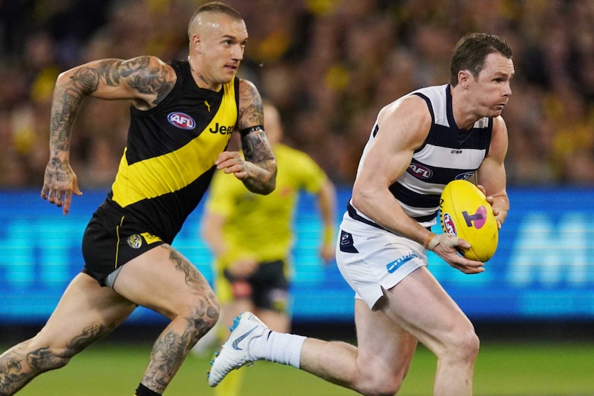 Patrick Dangerfield runs with the ball, while Dustin Martin and a few other players trail in his wake