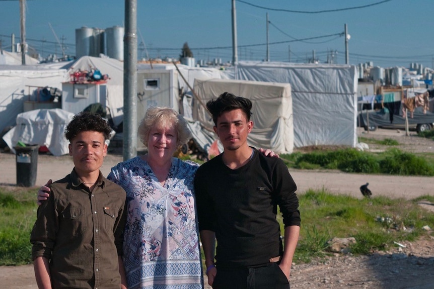 A woman with two young men standing in a refugee camp.