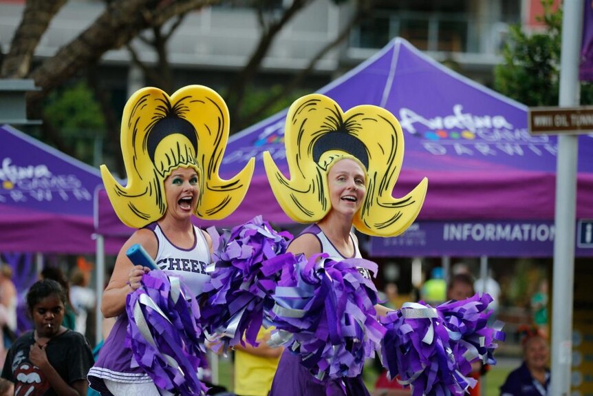 Women in cheerleading outfits pose, grinning.