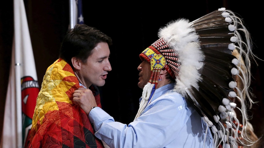 Assembly of First Nations National Chief Perry Bellegarde adjusts a blanket presented to Canada's Prime Minister Justin Trudeau