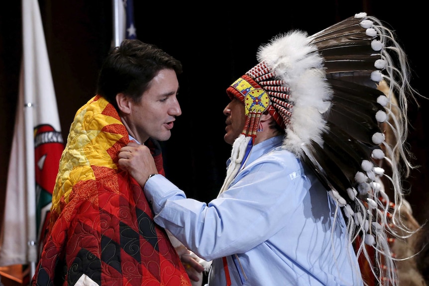 Assembly of First Nations National Chief Perry Bellegarde adjusts a blanket presented to Canada's Prime Minister Justin Trudeau